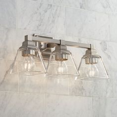 three light bathroom fixture with clear glass shades on the bottom and sides, against a white marble wall