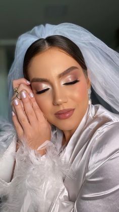 a woman in a white dress and veil holding her hands to her face while wearing a ring