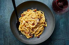 pasta with bacon and parmesan cheese in a bowl next to a glass of wine