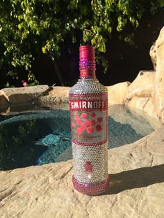 a bottle that is sitting on some rocks by the pool with trees in the background