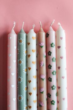 four candles are lined up against a pink wall with hearts and daisies on them