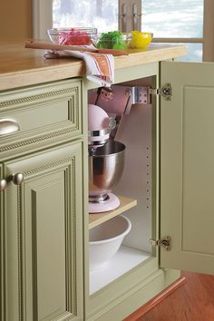 an open cabinet in the middle of a kitchen with bowls and utensils on it