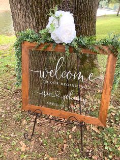 a welcome sign with flowers and greenery on it is sitting in front of a tree