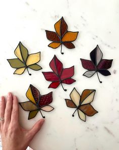 a hand is pointing at some stained glass leaves on a marble counter top, which are multicolored