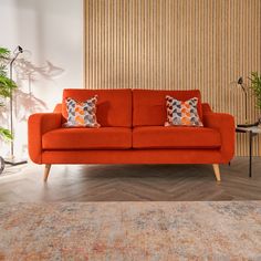 an orange couch with two pillows on it in front of a wooden paneled wall