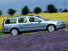 a silver car driving down a road next to a field of purple flowers and trees