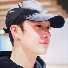 a young man wearing a black baseball cap and ear piercings, looking at the camera