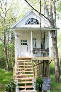 a small white house in the woods with stairs leading up to it's front door