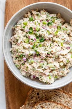 a white bowl filled with chicken salad on top of a wooden cutting board next to sliced bread