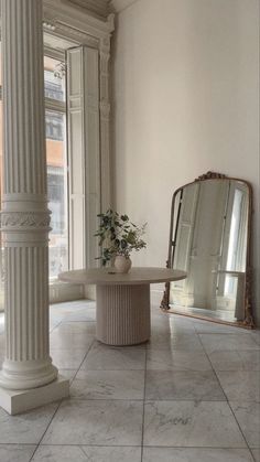 a white room with columns and a mirror on the wall, in front of it