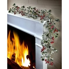 a white fireplace with red and green garland on it's mantle next to a fire