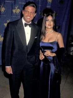 a man in a tuxedo standing next to a woman wearing a blue dress