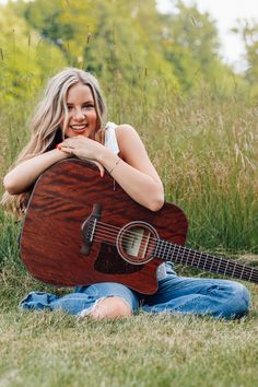 a woman sitting in the grass with an acoustic guitar and smiling at the camera,