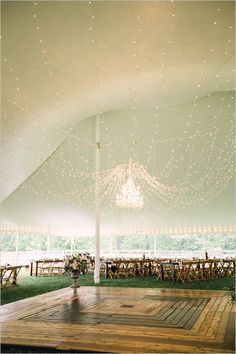 the inside of a tent with tables and chairs set up for a wedding reception under string lights