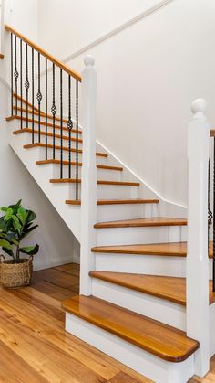 a white staircase with wooden handrails next to a potted plant