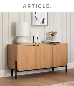 a wooden cabinet sitting next to a lamp on top of a hard wood floor in front of a white wall