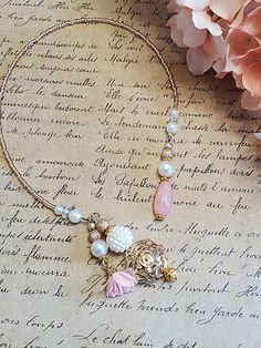 a necklace with charms and flowers on top of a piece of paper next to pink flowers