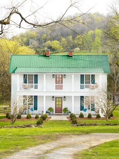 a white house with a green roof and red shutters on the front door is surrounded by trees