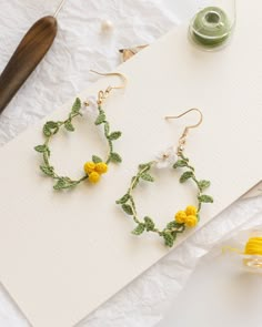 two pairs of yellow and white flowers are hanging from hoop earrings on a piece of paper