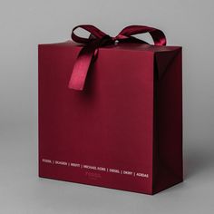 a red gift bag with a ribbon tied around the top and bottom, on a gray background