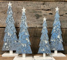 three metal christmas trees on display in front of a wooden background with white stars and scrolls