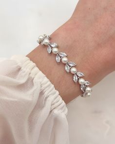 a woman's hand wearing a bracelet with white pearls and crystal stones on it