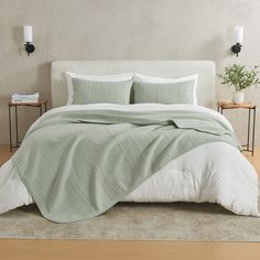 a bed with green and white comforters in a room next to two nightstands