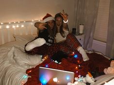 two young women sitting on a bed with christmas lights all around them and one is holding up the peace sign