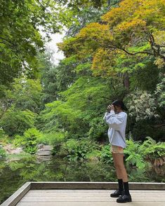 a woman standing on a deck in front of a pond taking a photo with her cell phone