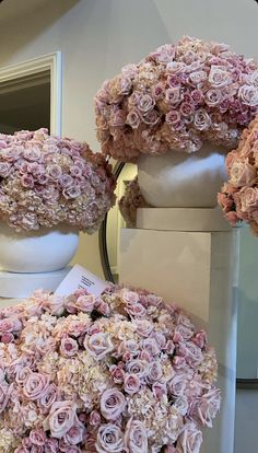 three white vases filled with pink flowers on top of a table next to each other