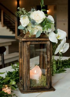 a wooden lantern with flowers and greenery on the table at a wedding or reception