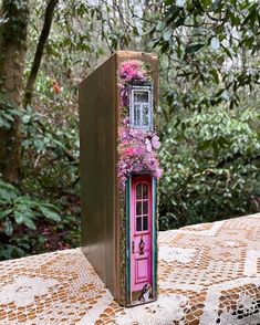 an open book with flowers on it sitting on a table in front of some trees