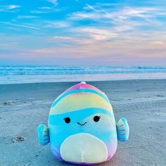 a stuffed toy sitting on top of a sandy beach next to the ocean at sunset