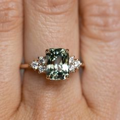 a woman's hand holding an engagement ring with a green and white diamond