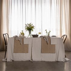 the table is covered with linens and has flowers in vases on each side