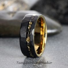 a black and gold wedding ring with an intricate design on it's side, sitting on top of a rock