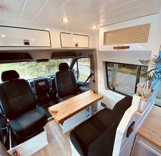 the interior of a camper with black seats and wood table in front of it