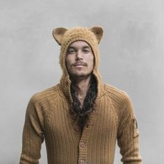 a man with long hair wearing a brown sweater and bear ears on his head is standing in front of a gray wall