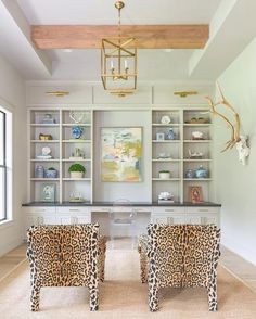 two leopard print chairs sitting in front of a white desk and bookshelf with open shelving