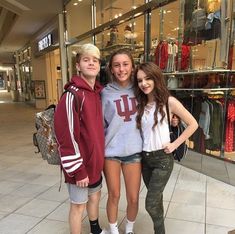 two girls and a boy standing in front of a clothing store with their arms around each other