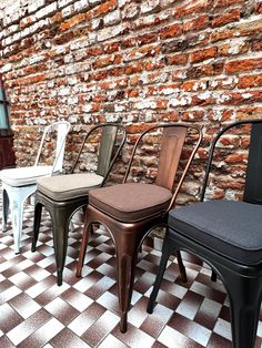 four different colored chairs sitting next to each other in front of a brick wall on a checkered floor