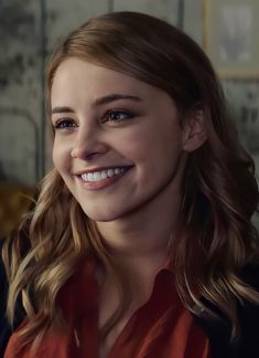 a close up of a person wearing a red shirt and looking at the camera with a smile on her face