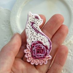 a hand holding a pink and white brooch in it's left hand, next to a plate