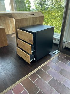 a black filing cabinet sitting on top of a hard wood floor next to a window