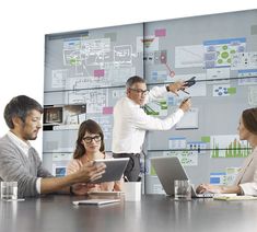 a group of people sitting around a table with laptops and papers on the wall