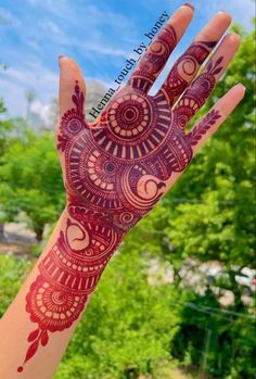 a person's hand with henna tattoos on it and trees in the background