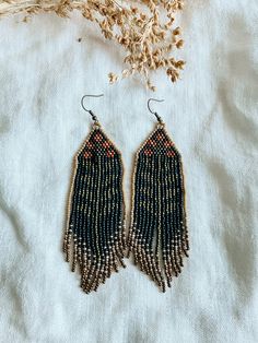 two pairs of beaded earrings with fringes on top of a white cloth next to dried flowers