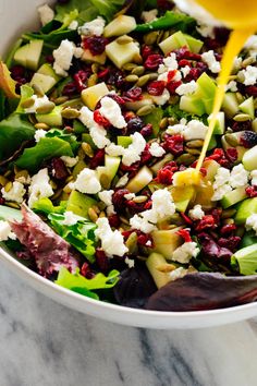 someone pouring dressing onto a salad in a white bowl on a marble countertop,