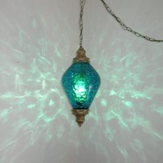 a green lamp hanging from a chain on a wall with light reflecting off it's side