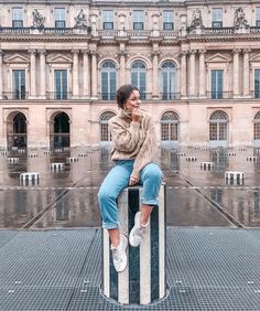 a woman sitting on top of a metal pole in front of a building with lots of windows